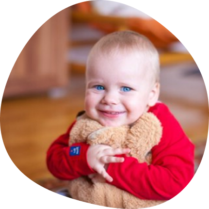 Smiling child in red hugging a teddy at Playful Scholars, Midland.