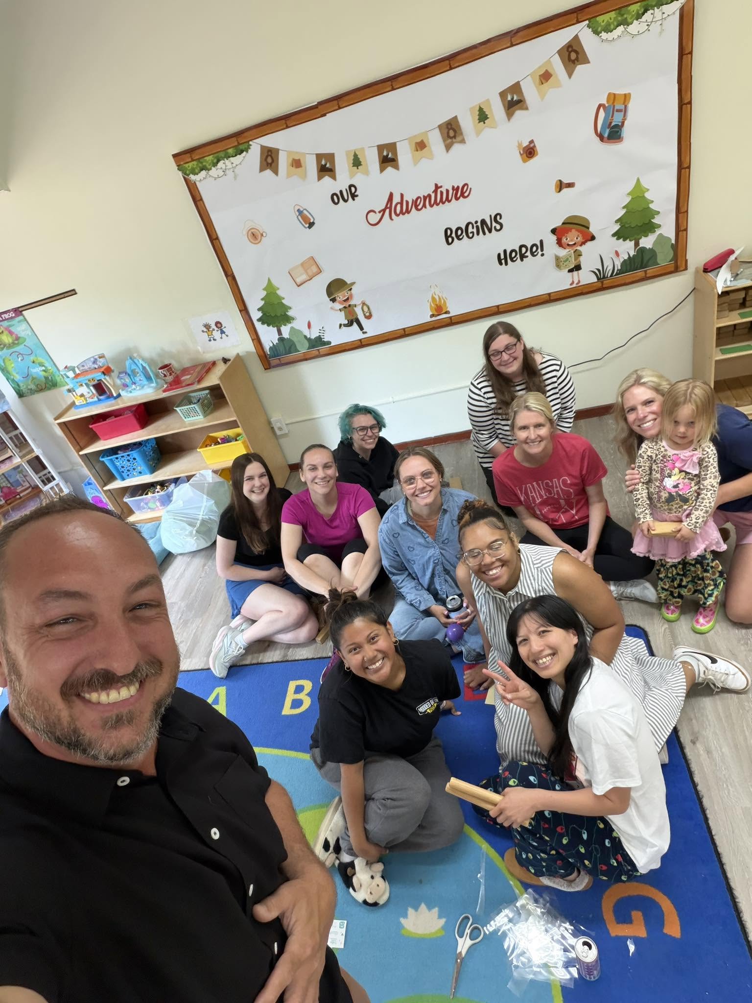 Educators at Playful Scholars preschool in Midland, MI gather on a colorful rug under a welcoming classroom banner.
